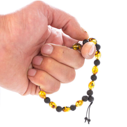 Brățară terapeutică din chihlimbar și pietre de lavă, ținută în mână, evidențiind mărimea și textura mărgelelor si faptul ca poate fi folosita pentru rostirea afirmatiilor